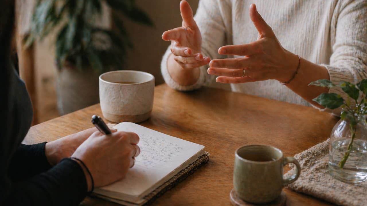 Intiem coachgesprek met focus op handen, notitieboek en thee tijdens persoonlijke begeleiding